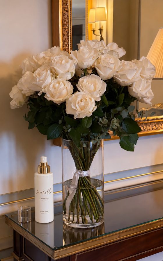 Home spray Presença junto a um ramo de rosas brancas numa consola